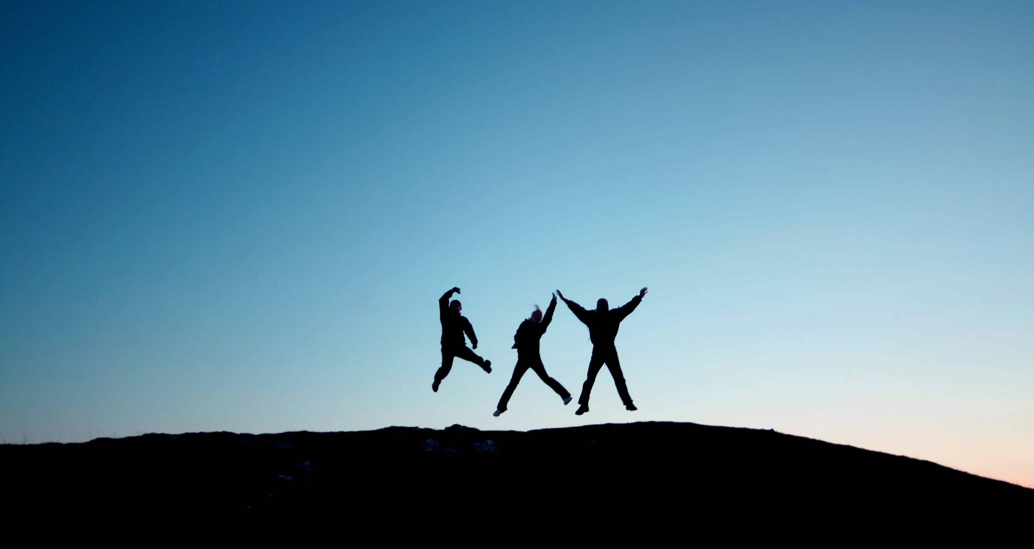Three people silhouetted jumping for joy at sunset, picturing believers' freedom in Christ
