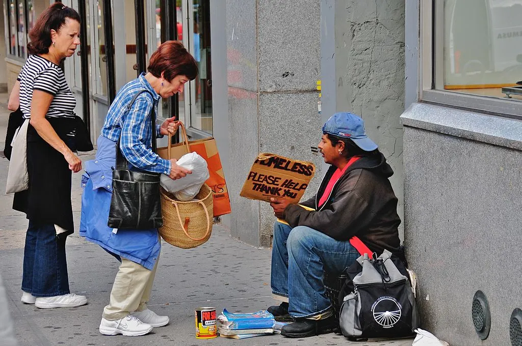 Women giving food to a homeless man on a city street, an act of kindness and good works