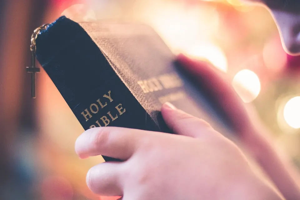 Hand holding a black leather Holy Bible, the Word of God
