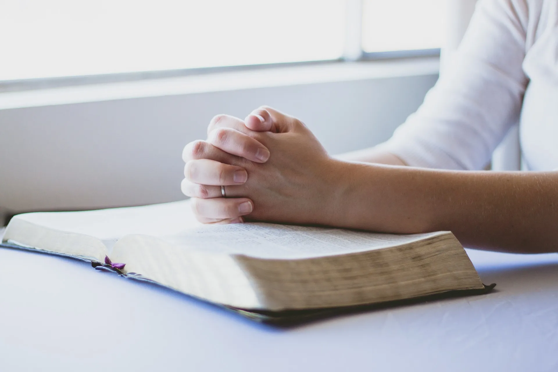 Hands folded in prayer over an open Bible