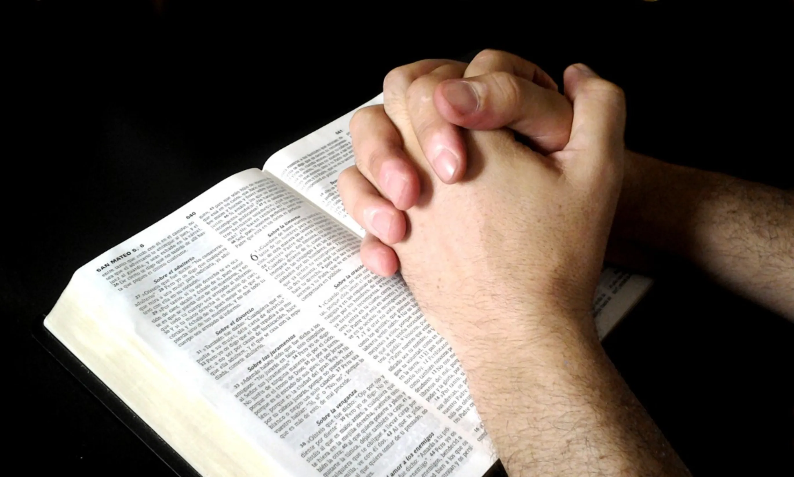 Clasped hands resting on an open Bible in prayer