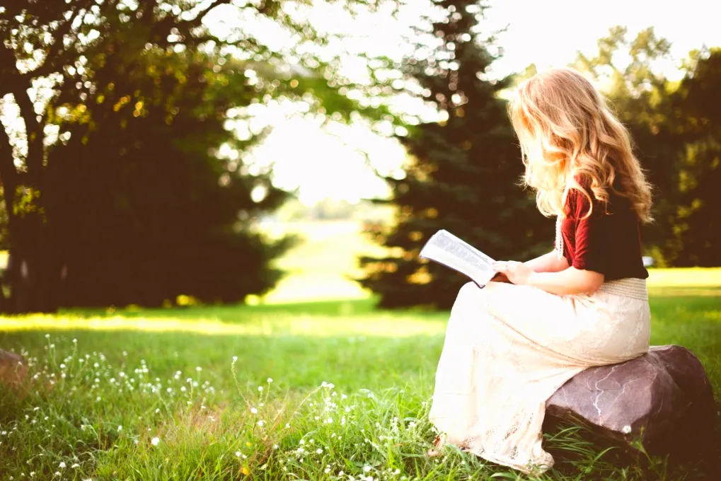 Young woman reading a devotional outdoors in the sunlight