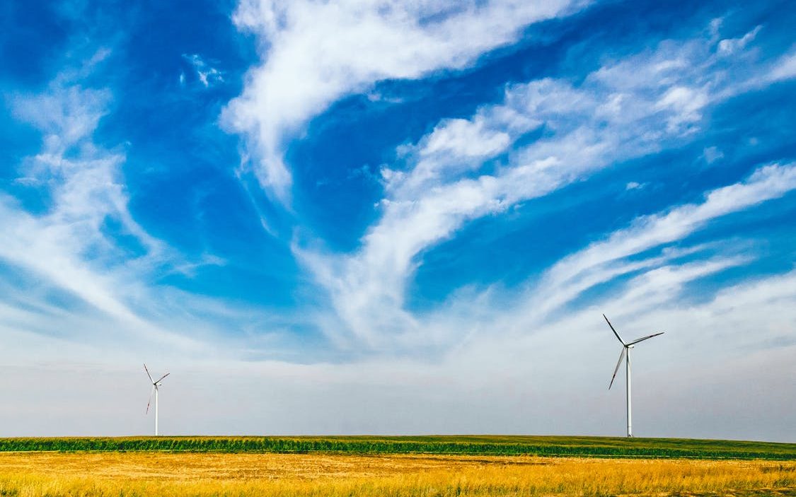 A plain with a windmill and cloud streaks in the sky caused by the wind, which goes where it pleases, like how the Holy Spirit gives gifts to believers